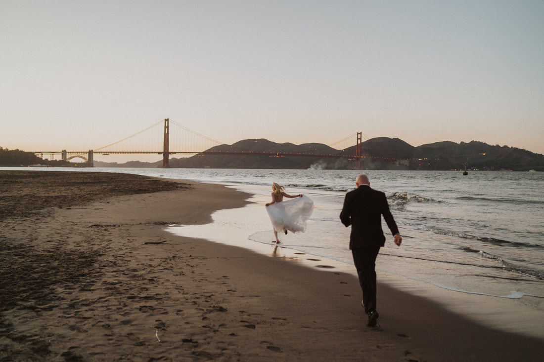 Couple running on the beach looking at the golden gate bridge during their San Francisco elopement 
